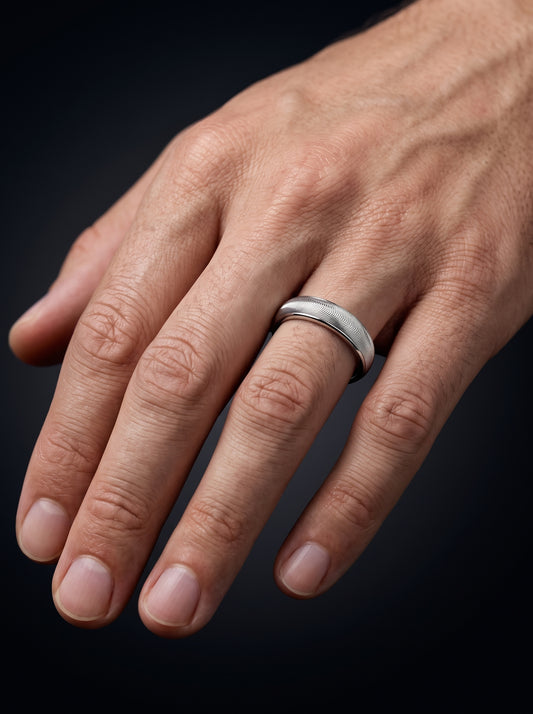 A close-up of a man's hand wearing a wave textured platinum band ring against a dark background.