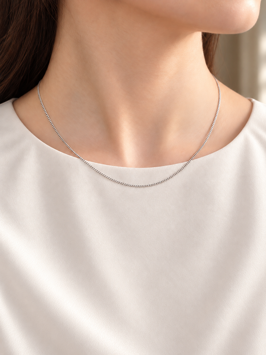 HELIOR Cadence Fine 1.6mm solid PT950 platinum curb chain necklace worn with a cream blouse, showing its fine scale and natural drape.
