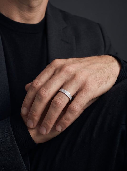 Man wearing the Dune frosted platinum band on his ring finger, with relaxed hands against dark tailoring.