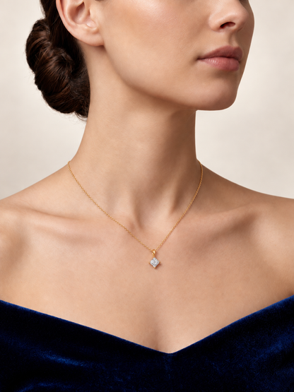 A close-up of a model wearing a delicate gold chain necklace with a small diamond pendant. The model is wearing a dark blue velvet off-the-shoulder top against a neutral beige background.