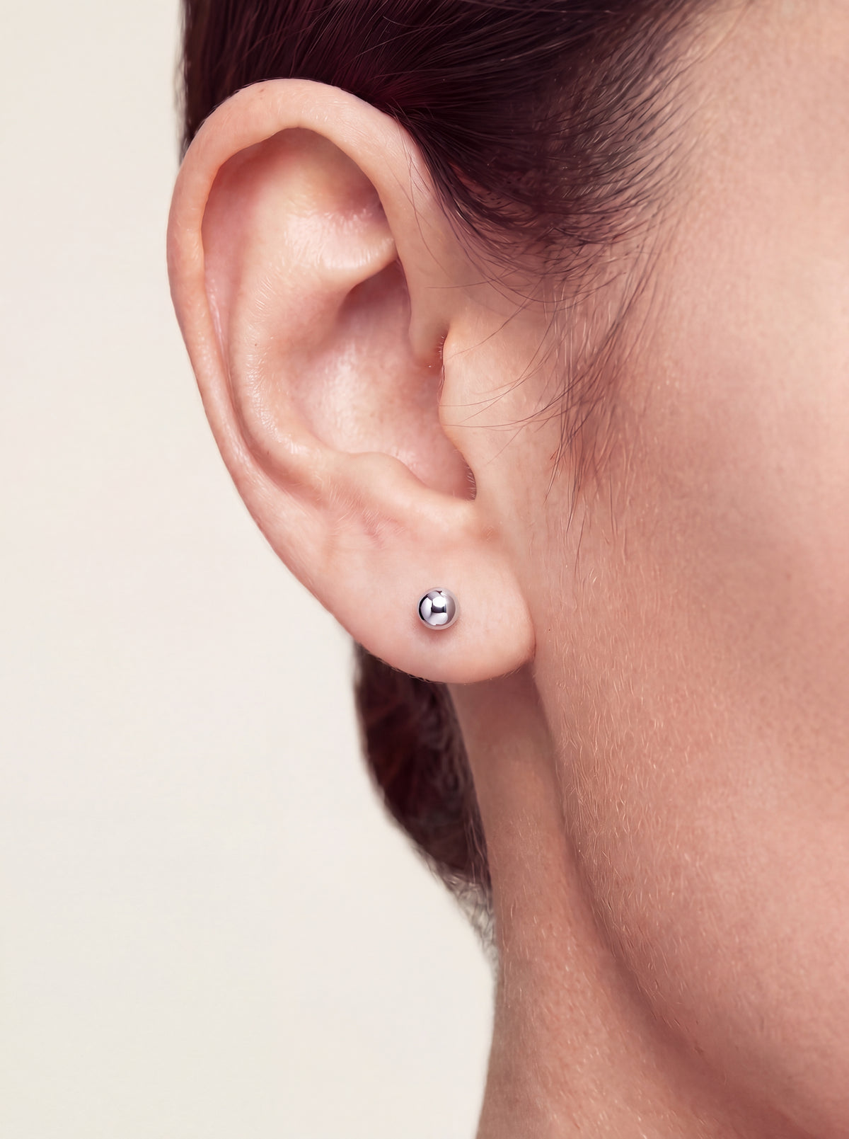 A close-up of a person's ear wearing a small platinum stud earring with a polished metallic sphere detail.