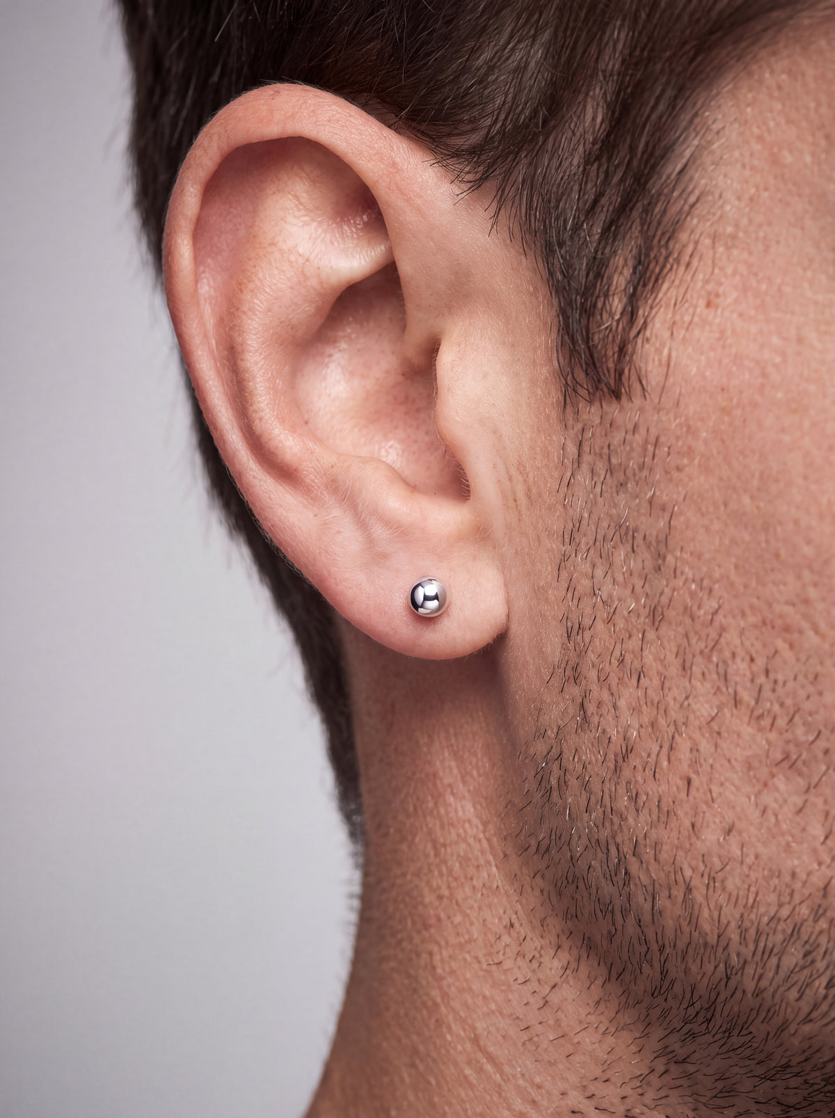 A close-up of a man's ear wearing a small, polished platinum  stud earring.