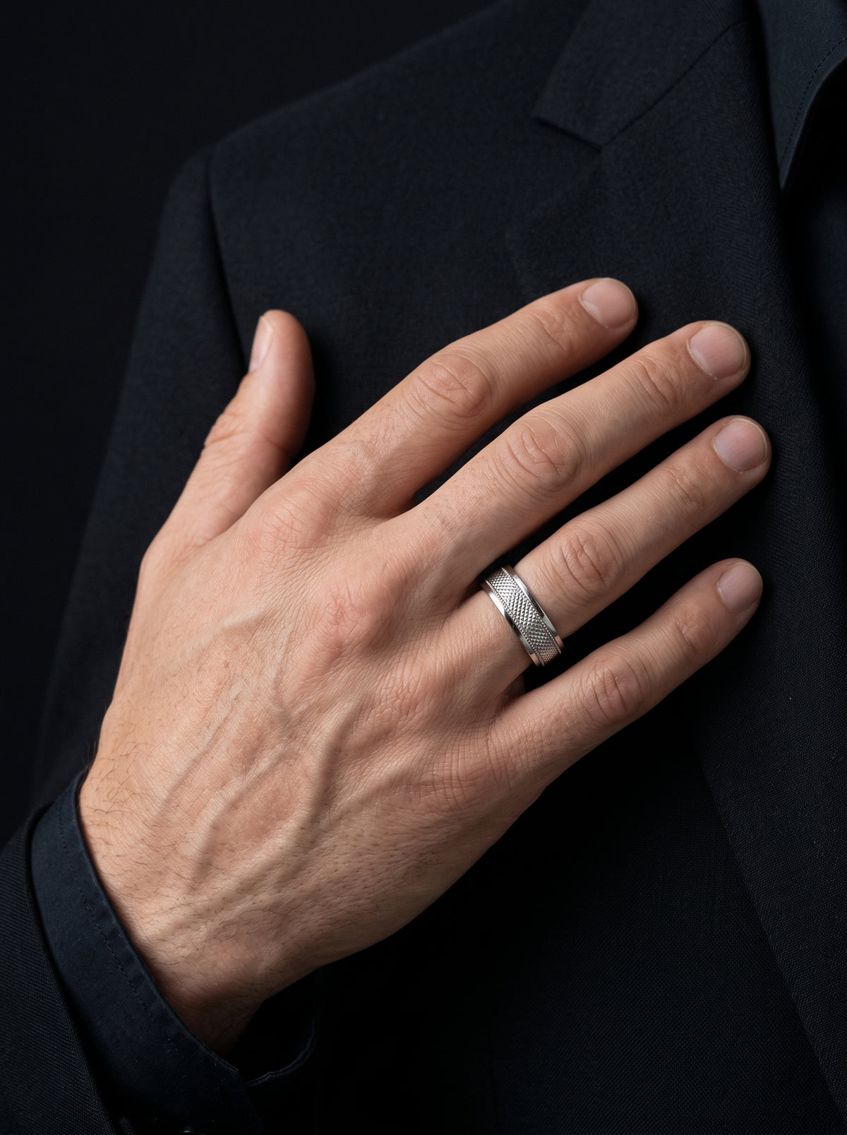 Close-up of a man wearing the HELIOR Clous platinum band against a black tailored jacket.