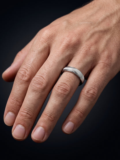 A close-up of a man's hand wearing a wave textured platinum band ring against a dark background.