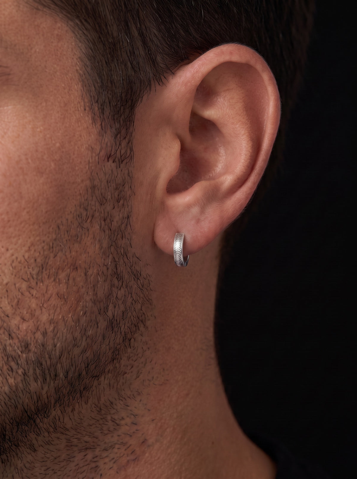 Vela textured platinum huggie hoop worn close to a man's earlobe