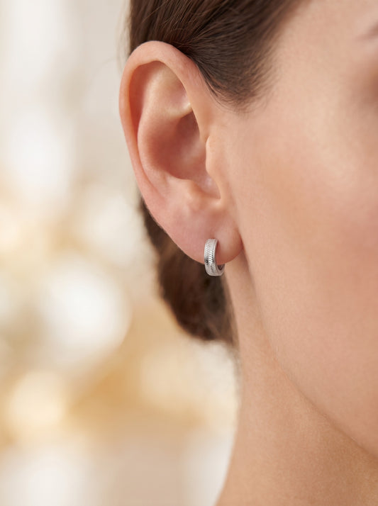 Vela textured platinum huggie hoop worn close to a woman's earlobe