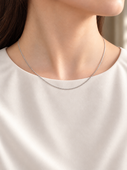 HELIOR Cadence Fine 1.6mm solid PT950 platinum curb chain necklace worn with a cream blouse, showing its fine scale and natural drape.