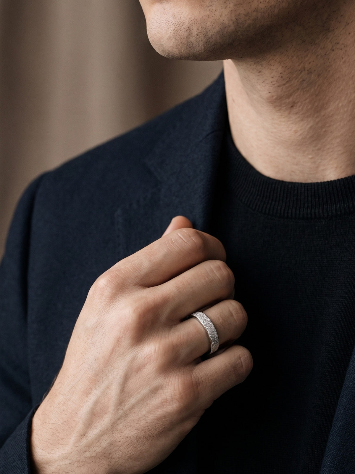 Dune frosted platinum band worn by a man holding his jacket lapel, showing the ring from an angled view.