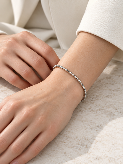HELIOR Orbit platinum faceted bead bracelet worn on a wrist resting on pale stone, with an ivory sleeve.