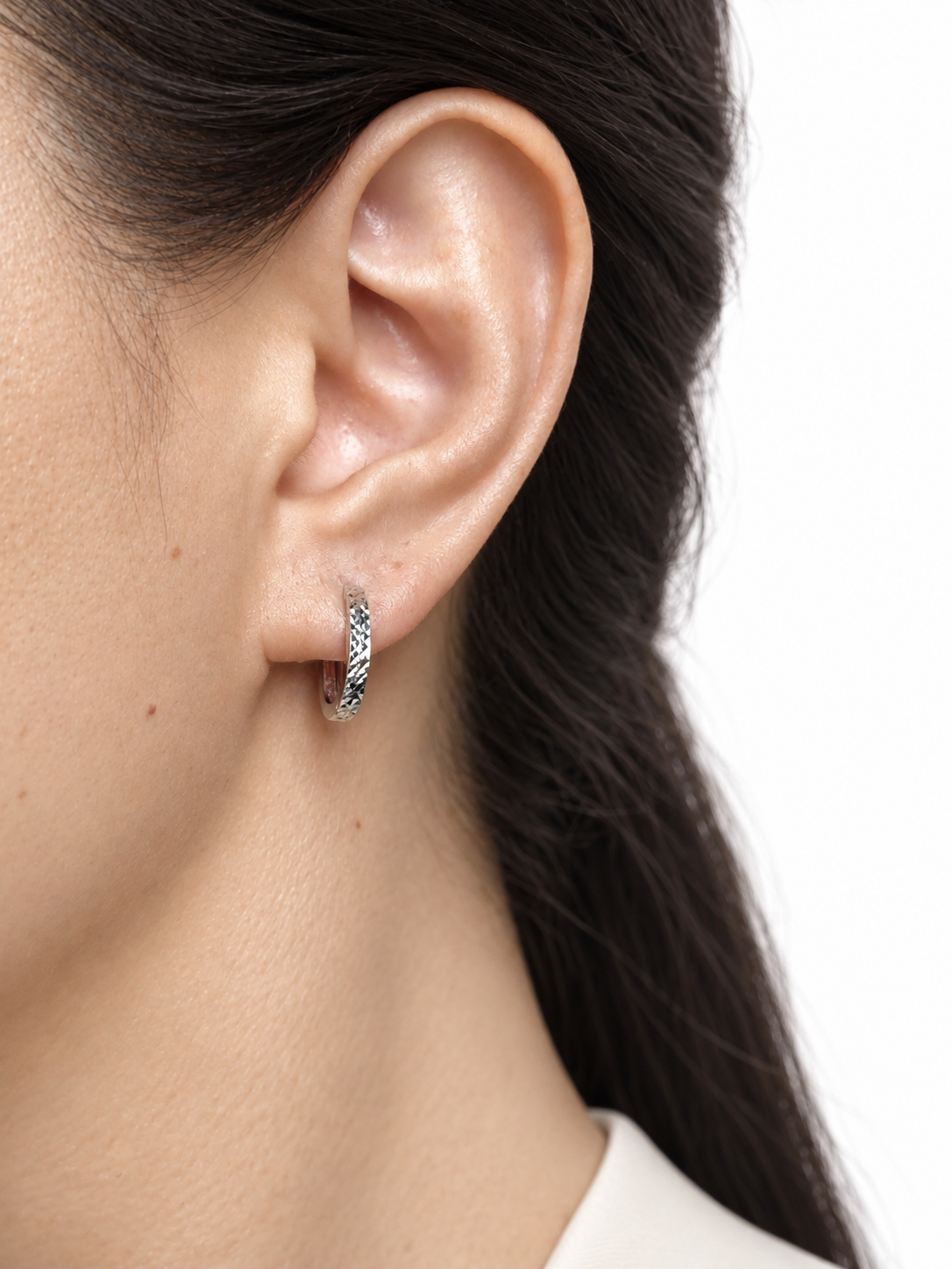 Woman wearing a HELIOR platinum faceted hoop earring with a light outfit