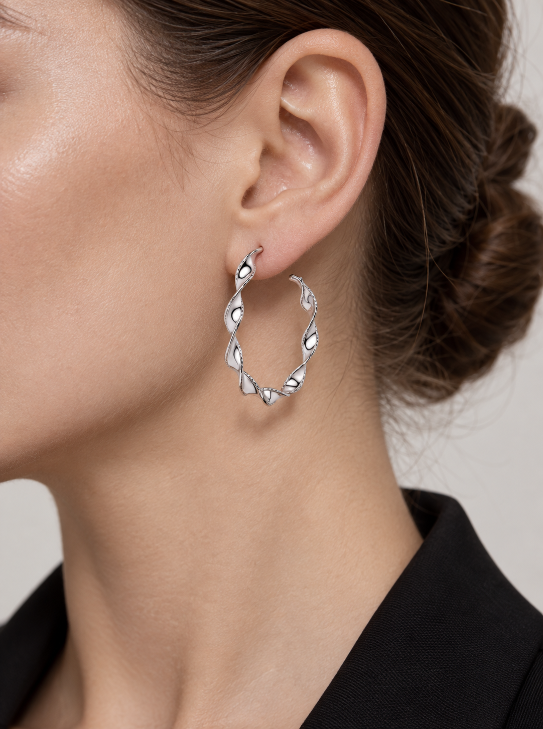 Platinum ribbon twist hoop earring worn close up with a black jacket