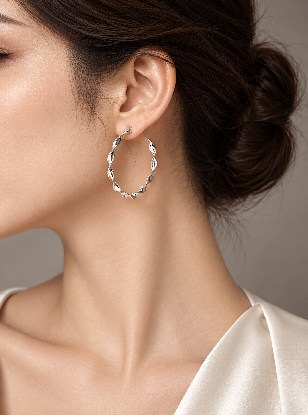 Platinum ribbon twist hoop earring worn with an ivory blouse