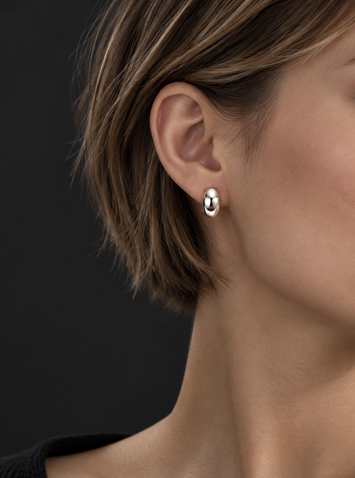 Close-up of a HELIOR PT950 platinum moon stud earring on an ear with a dark outfit and background