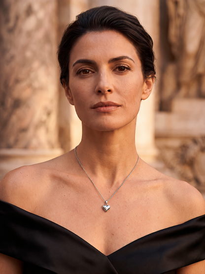 Model wearing the HELIOR platinum puffed heart pendant with a black off-the-shoulder dress in warm outdoor light.