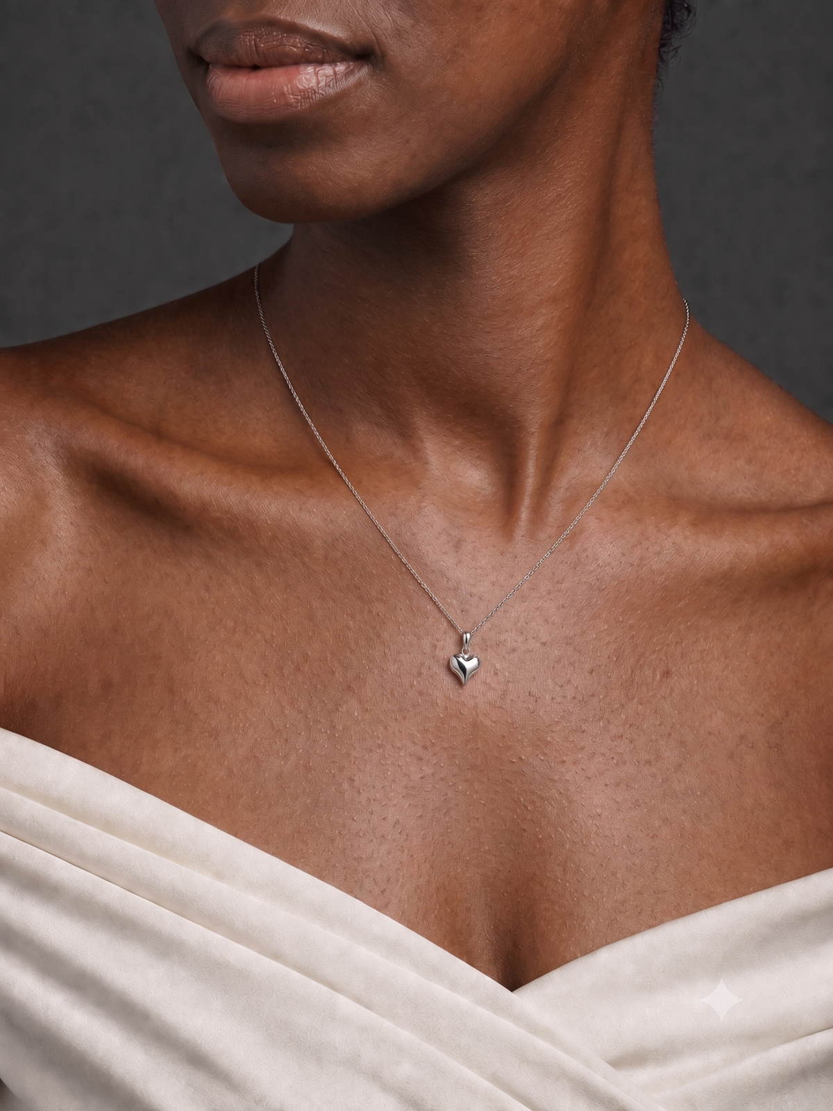Close-up of a model wearing the HELIOR platinum puffed heart pendant with a white neckline; chain not included.