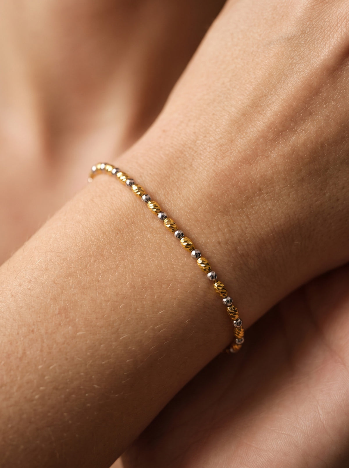Tempo two-tone gold bracelet worn around the wrist, showing its delicate alternating elongated and round faceted beads.