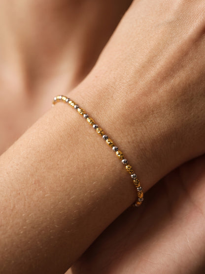 Tempo two-tone gold bracelet worn around the wrist, showing its delicate alternating elongated and round faceted beads.
