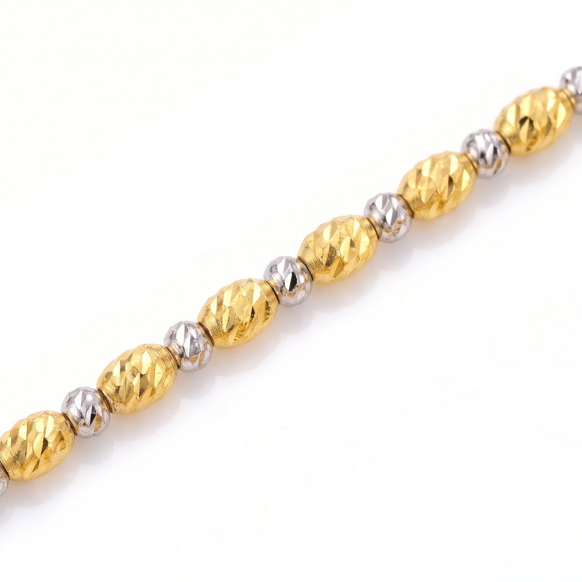 Macro detail of Tempo's elongated gold beads and small white-coloured beads, showing the diamond-cut surface texture.
