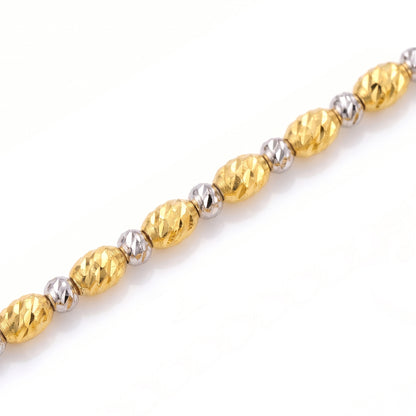 Macro detail of Tempo's elongated gold beads and small white-coloured beads, showing the diamond-cut surface texture.