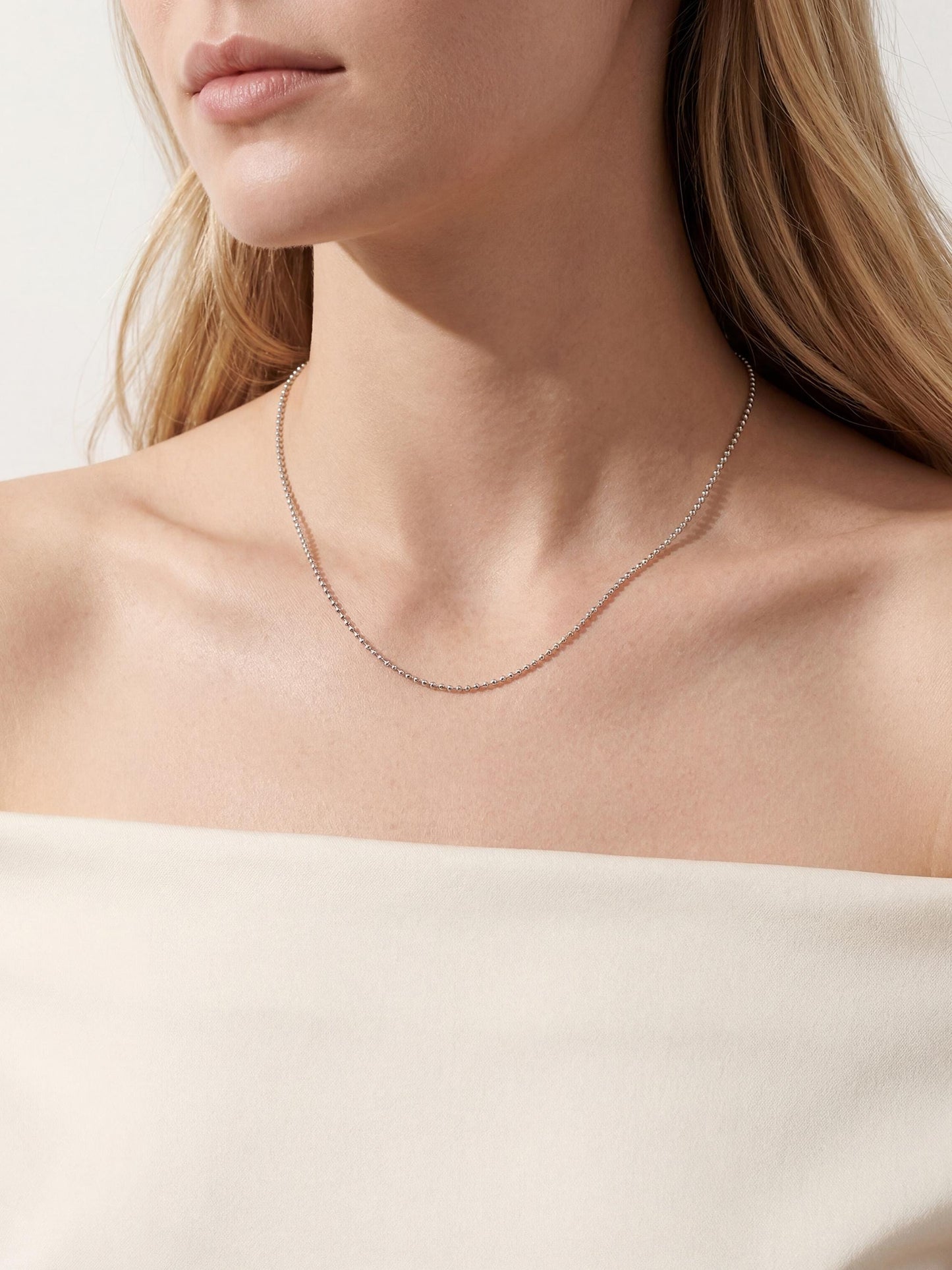 Woman wearing fine platinum bead chain with off-white off-shoulder top