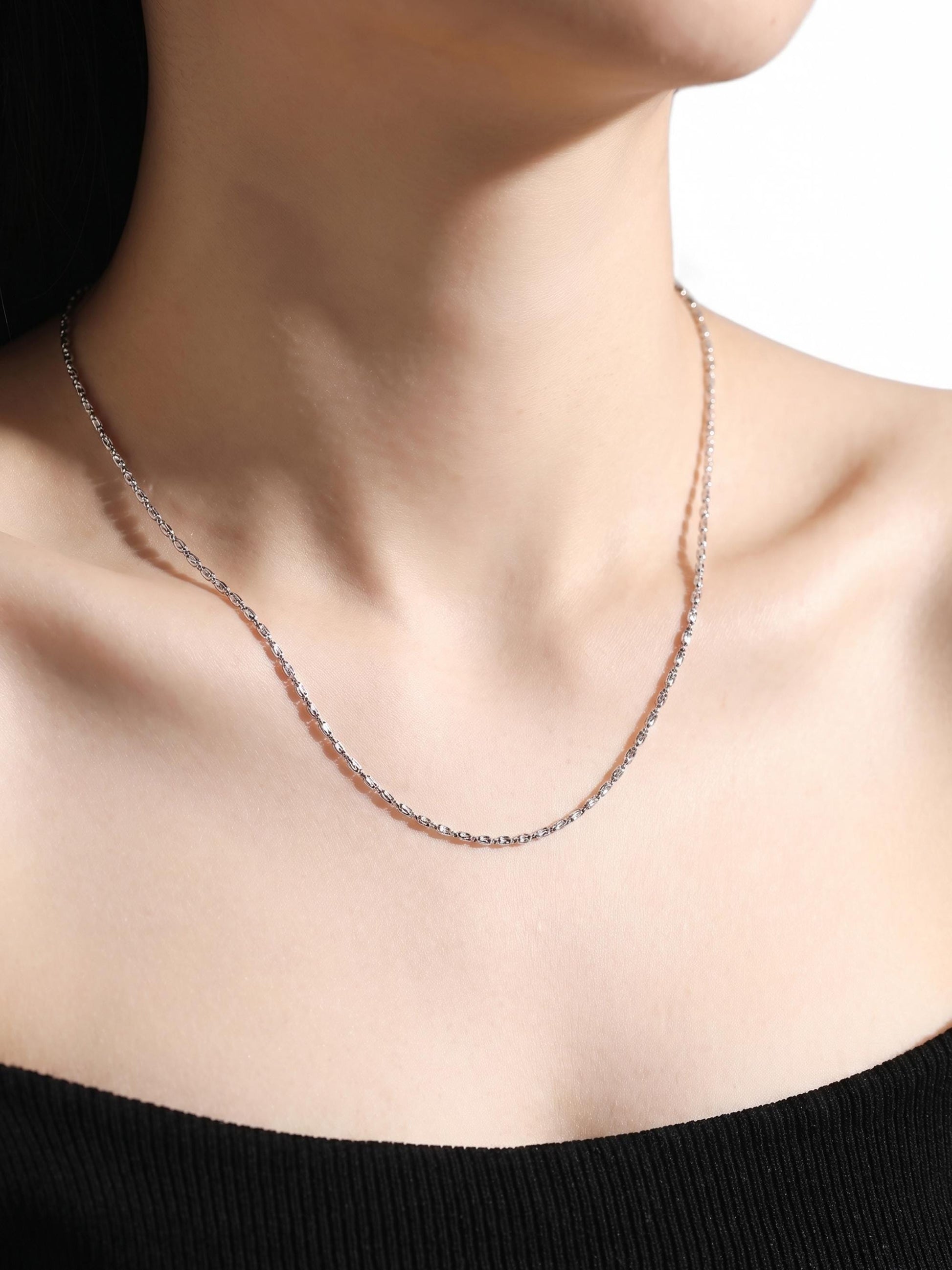 Woman wearing laser-cut platinum olive bead chain with black neckline