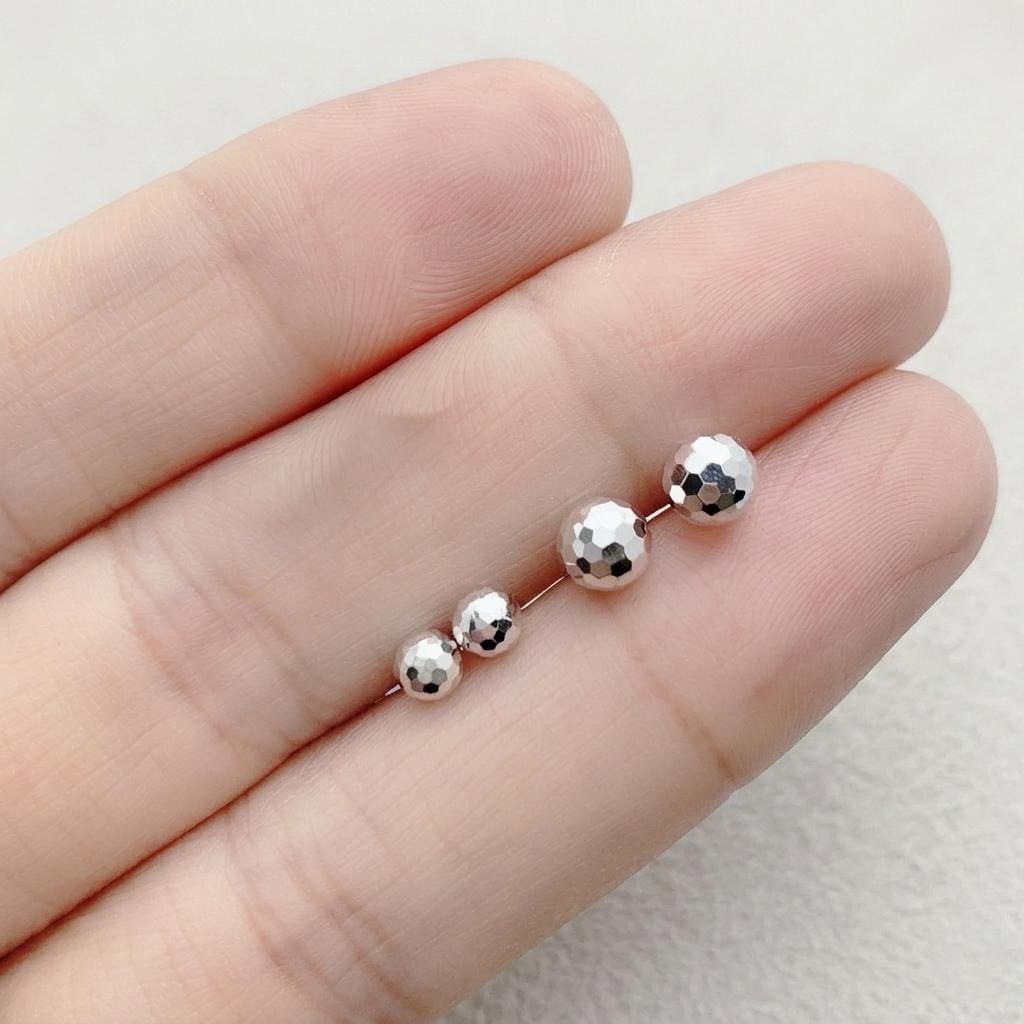 PT950 faceted ball stud earrings shown on fingertips