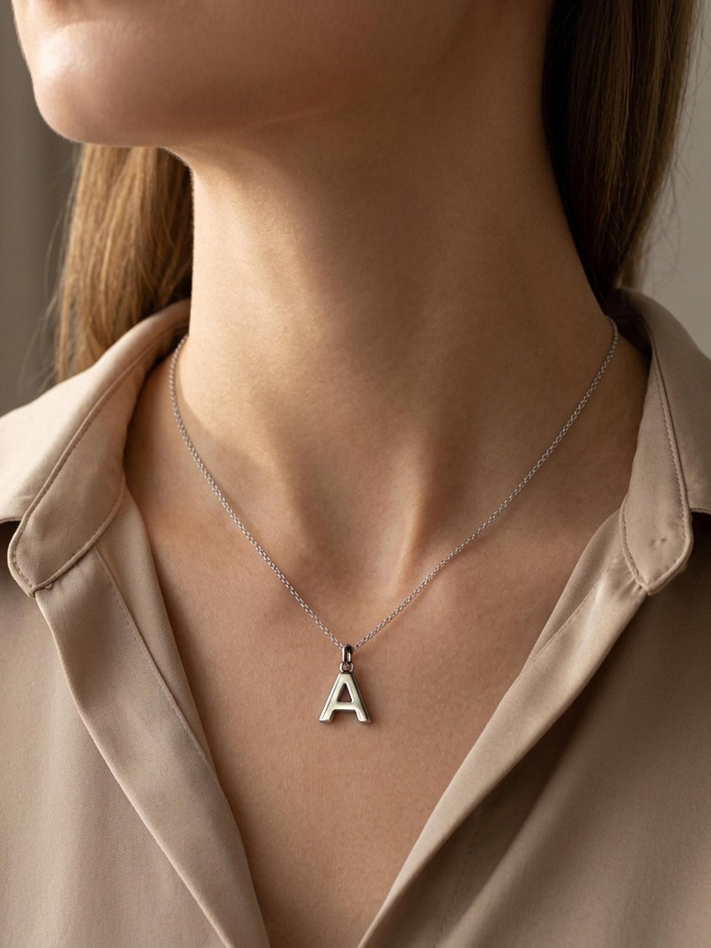 Woman wearing PT950 platinum initial necklace with beige blouse
