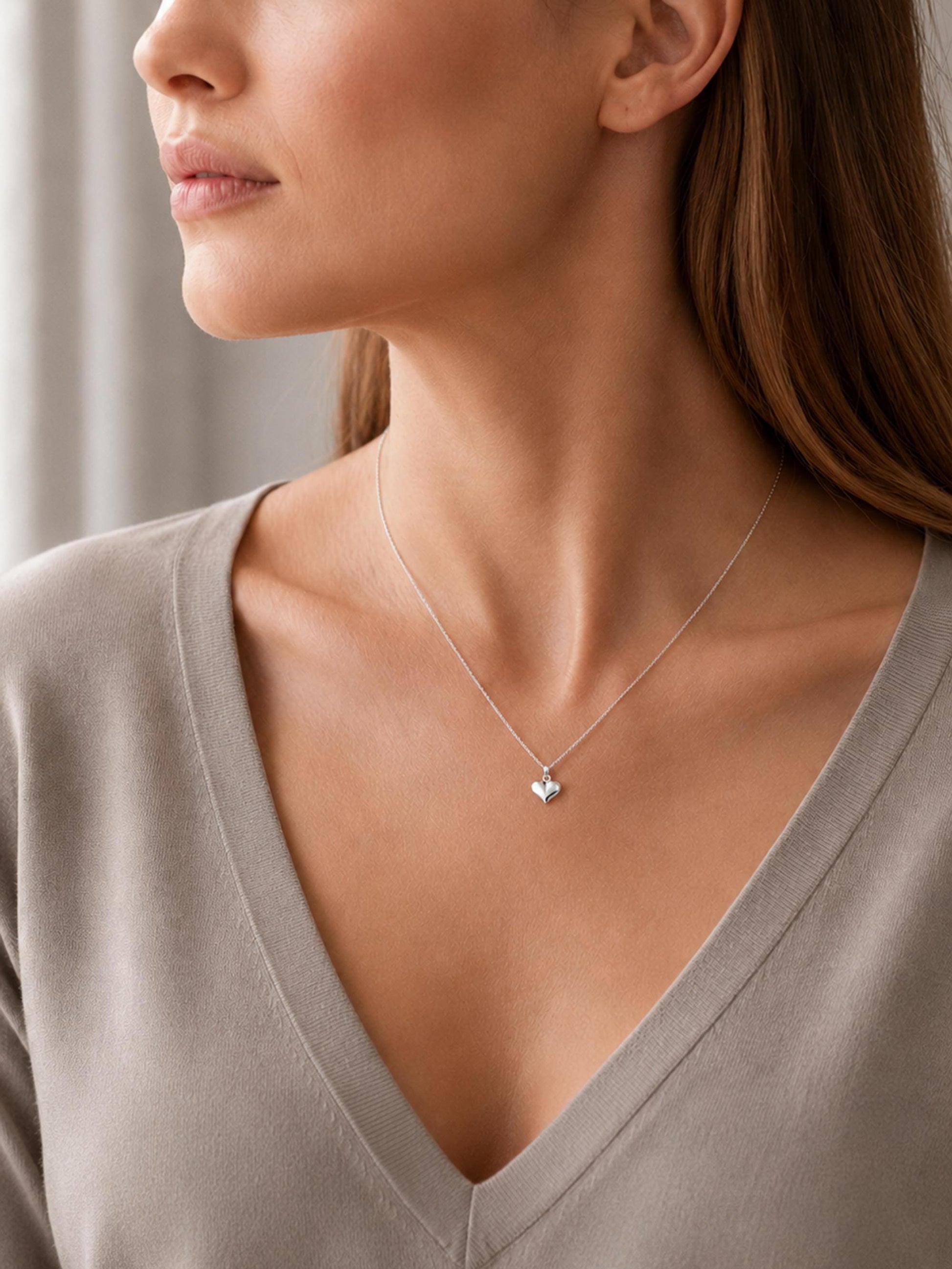 Woman wearing polished platinum heart necklace with taupe V-neck