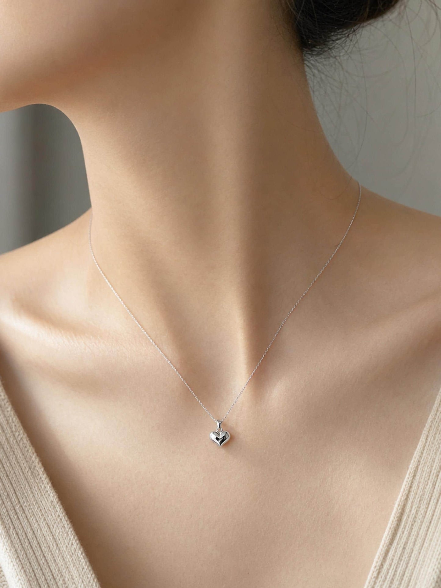 Woman wearing 10.6mm PT950 platinum heart pendant with beige knit neckline