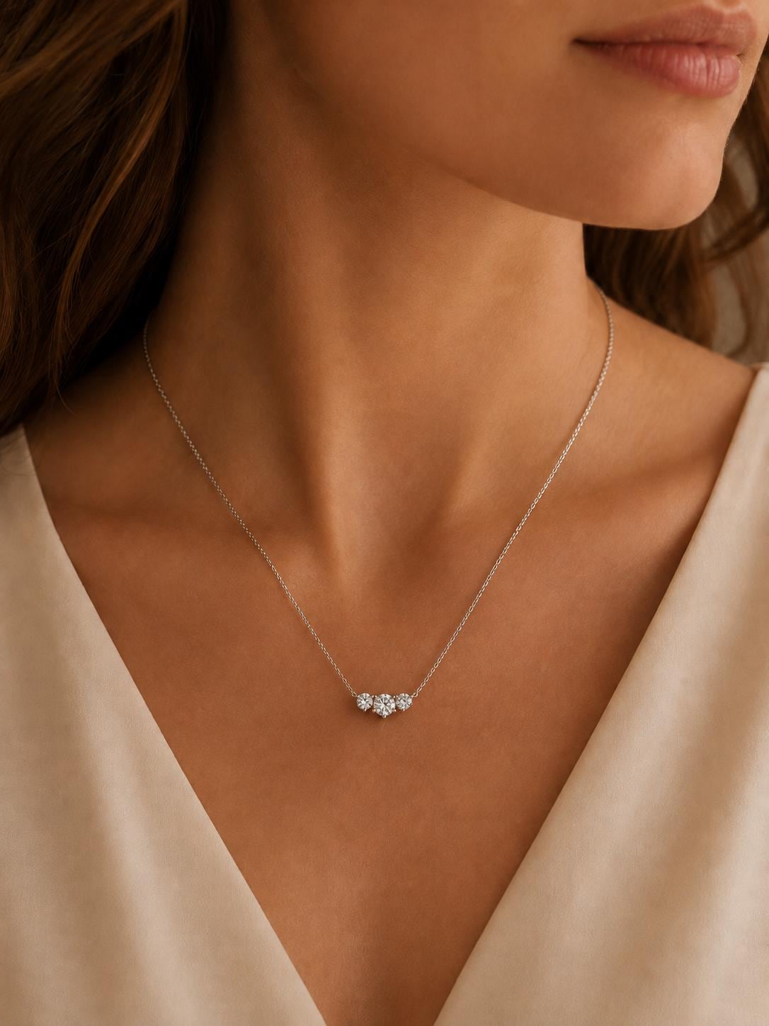 Woman wearing three-stone lab diamond pendant with cream V-neck