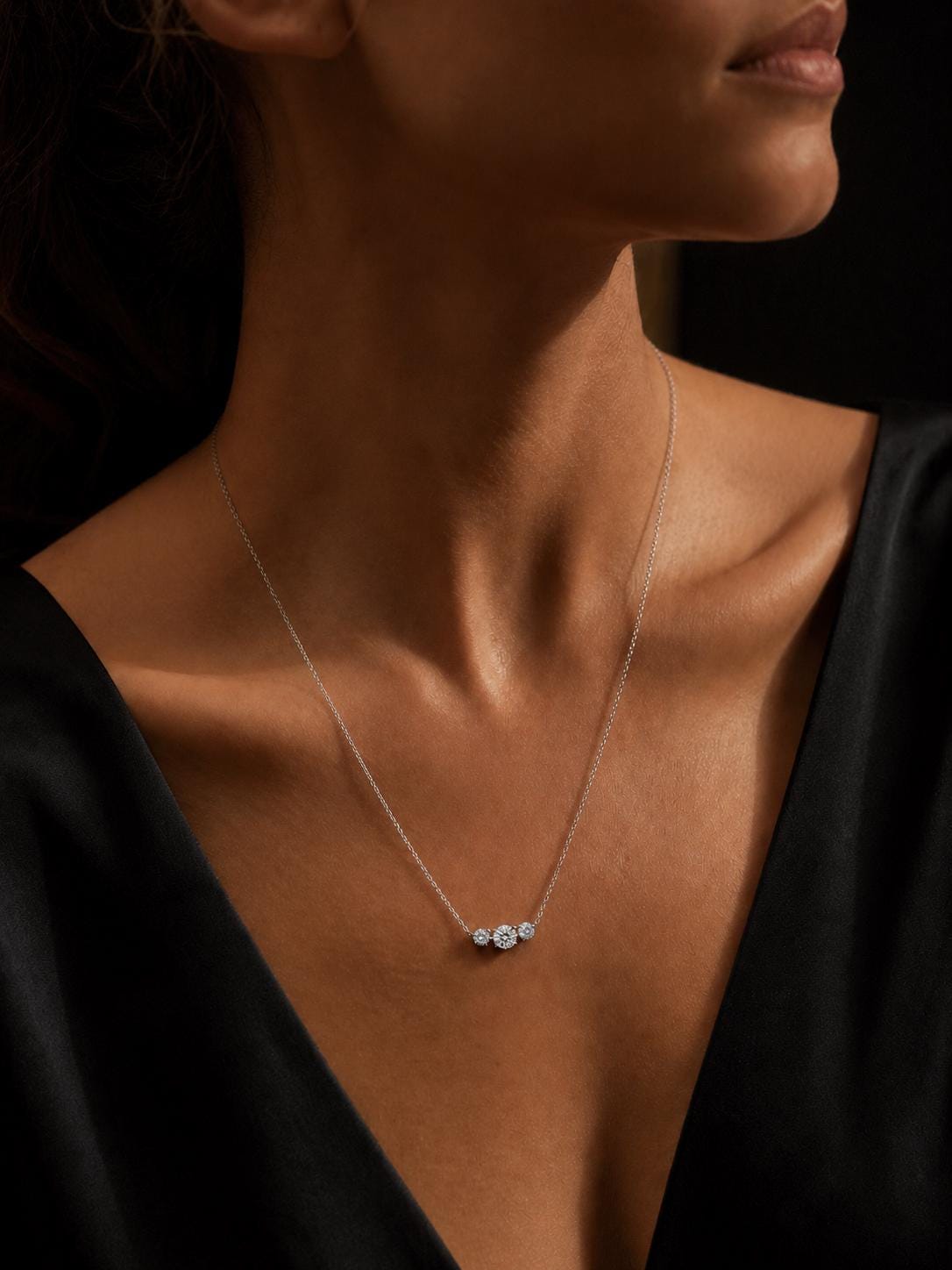 Woman wearing platinum three-stone diamond necklace at longer length