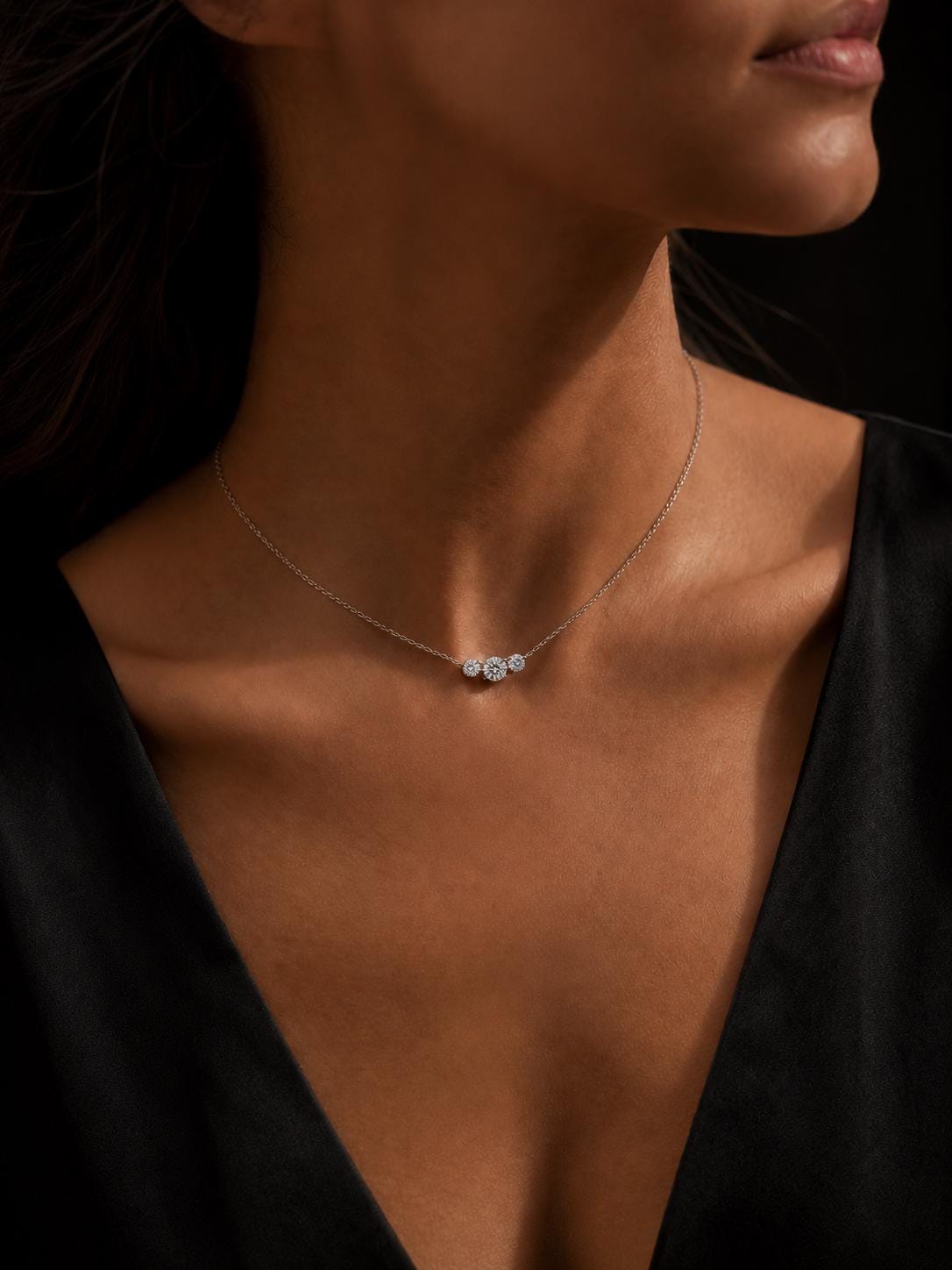 Woman wearing three-stone lab diamond necklace with low black V-neck