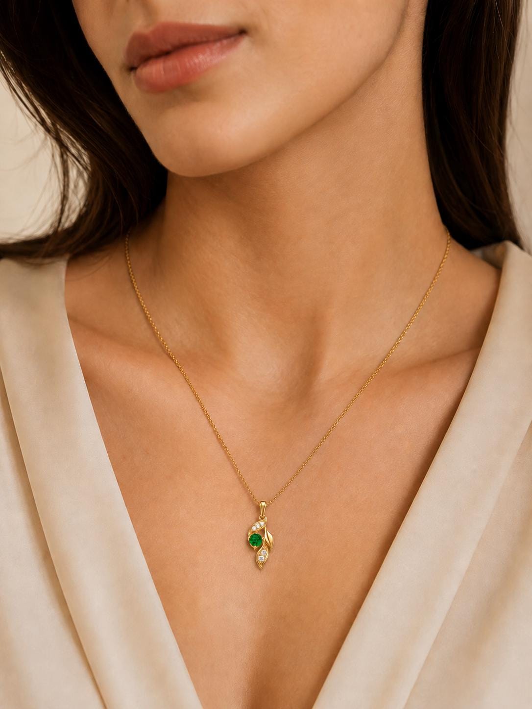 Woman wearing 18K gold emerald leaf pendant with cream V-neck
