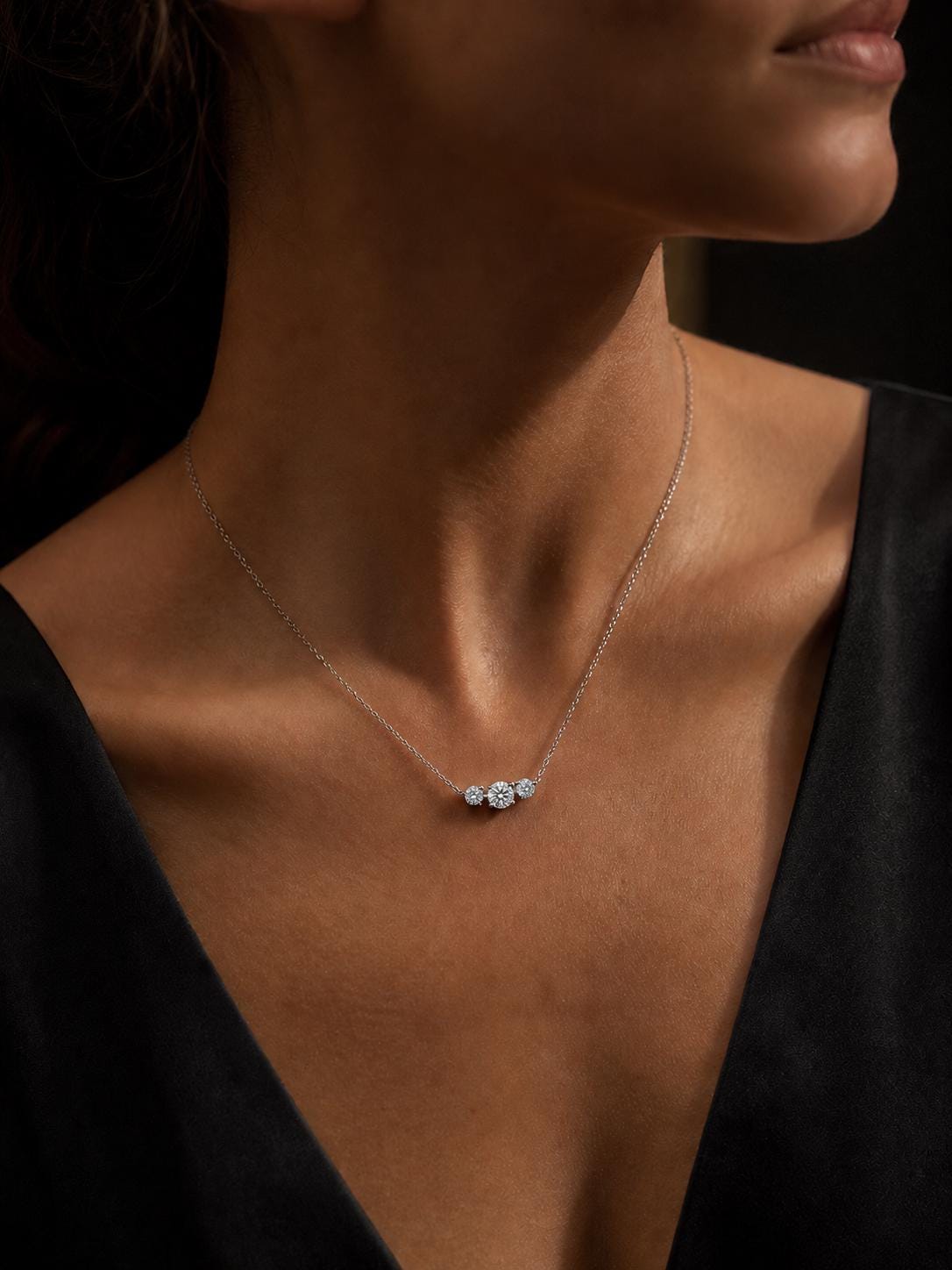Woman wearing platinum three-stone diamond necklace with black V-neck