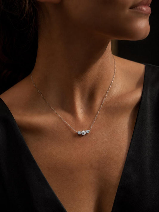 Woman wearing platinum three-stone diamond necklace with black V-neck
