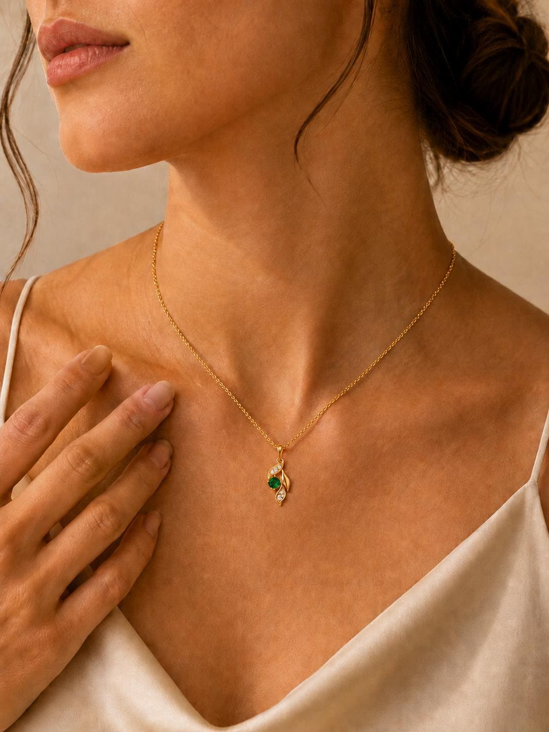 Close neckline view of emerald and diamond leaf pendant on cream satin