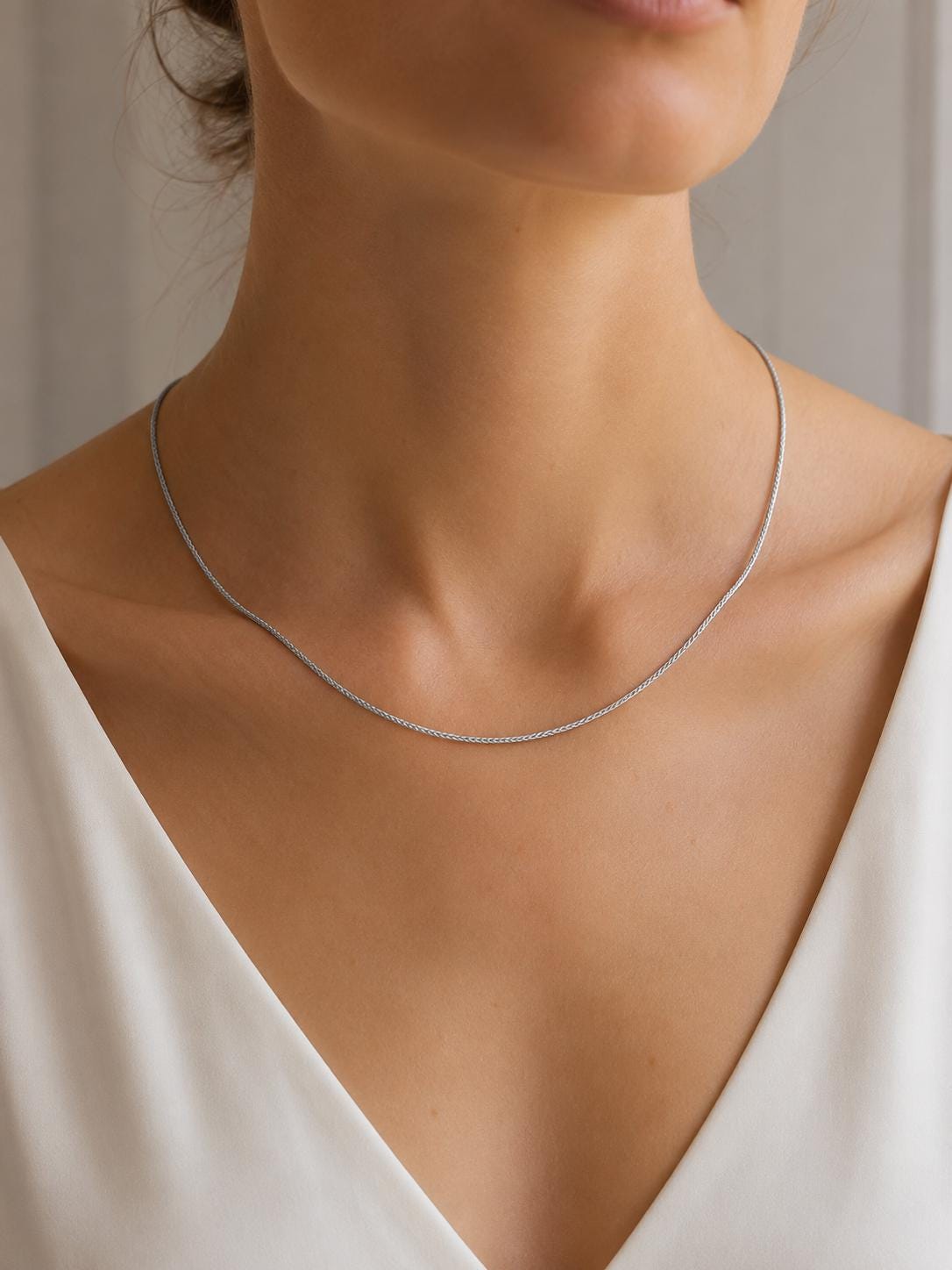 Woman wearing fine platinum wheat chain against a white neckline