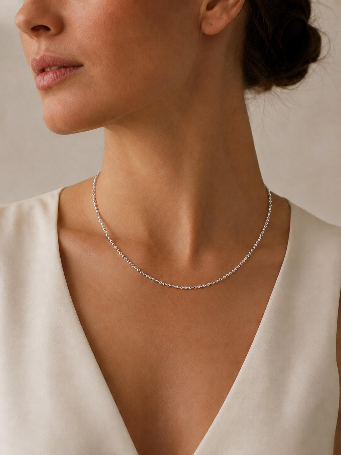 Woman wearing fine platinum diamond-cut bead necklace with cream V-neck