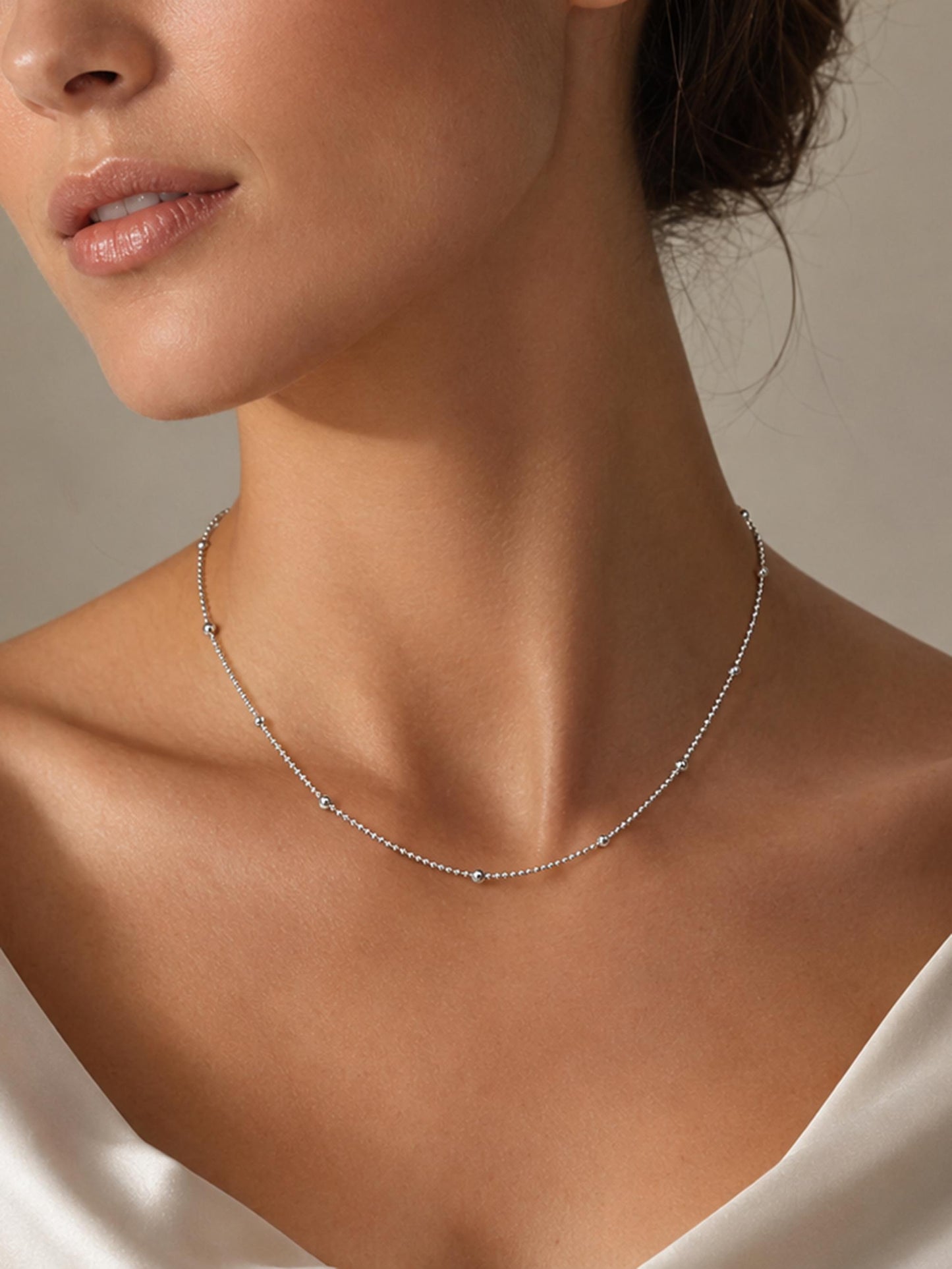 Woman wearing 45cm PT950 platinum station necklace with cream satin neckline