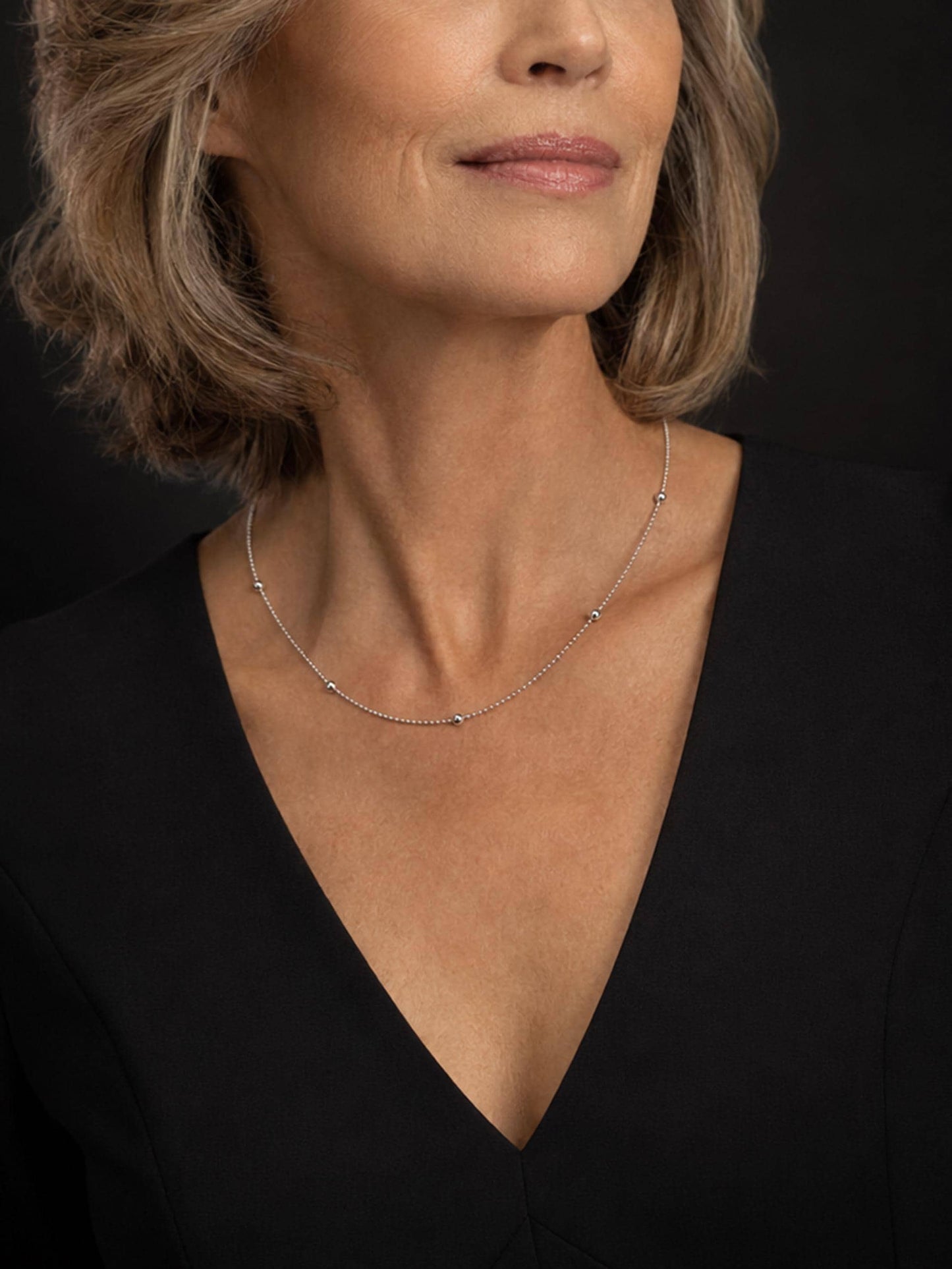 Mature woman wearing PT950 platinum station necklace with black V-neck