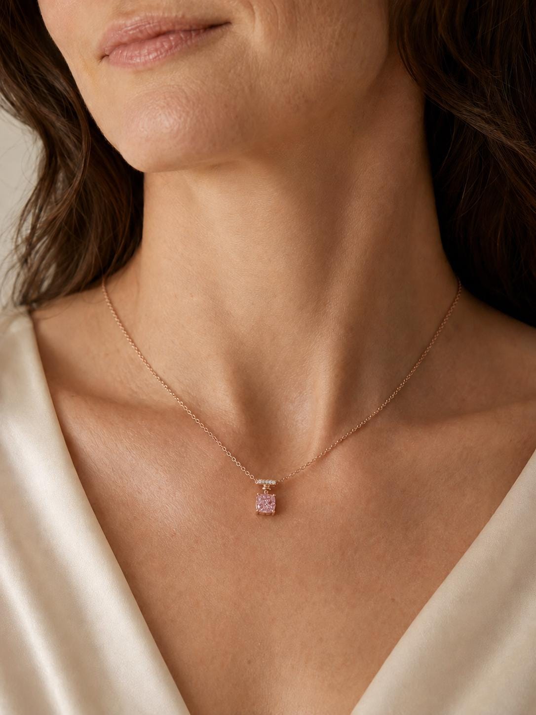 Woman wearing cushion pink diamond pendant with cream satin neckline