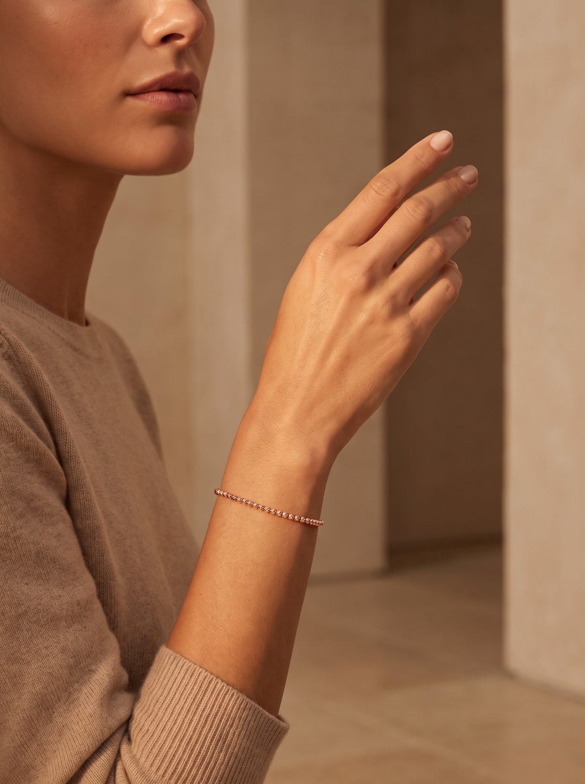 HELIOR Lustre 18K rose gold bead bracelet worn on a raised wrist in warm natural light.