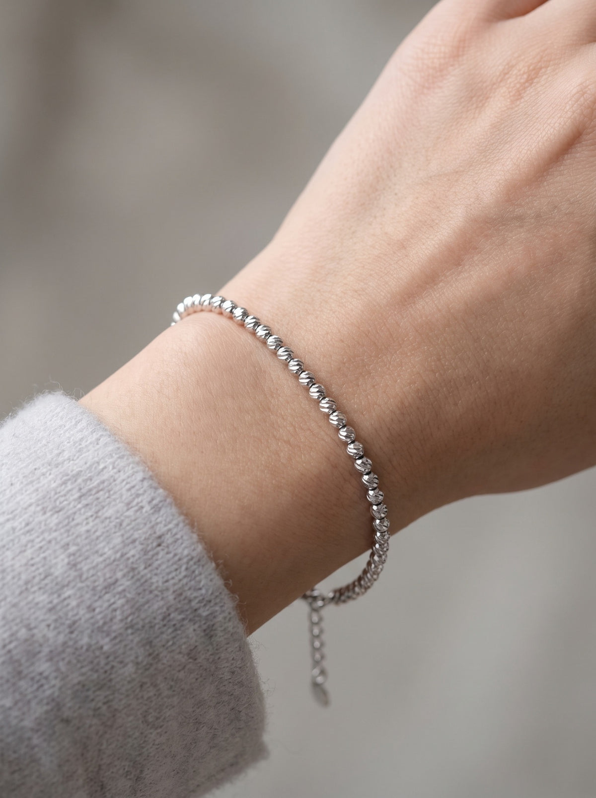 HELIOR Lustre 18K white gold bracelet with 3mm faceted beads worn on the wrist beside a soft knit cuff.